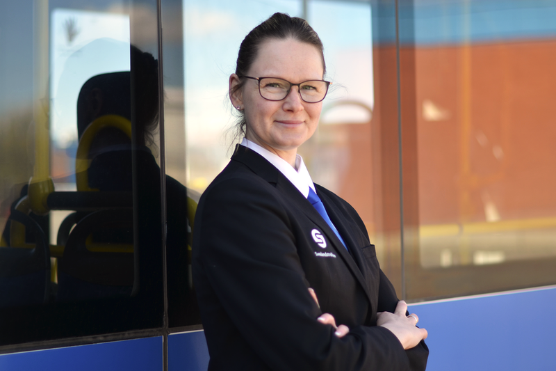 Porträttbild Marina Lorek, kvinnlig bussförare, buss i bakgrunden